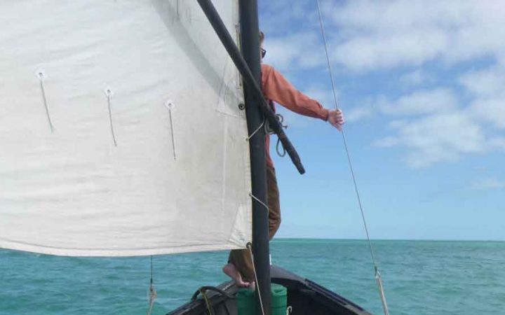 a person stands at the front of a sailboat holding a rope